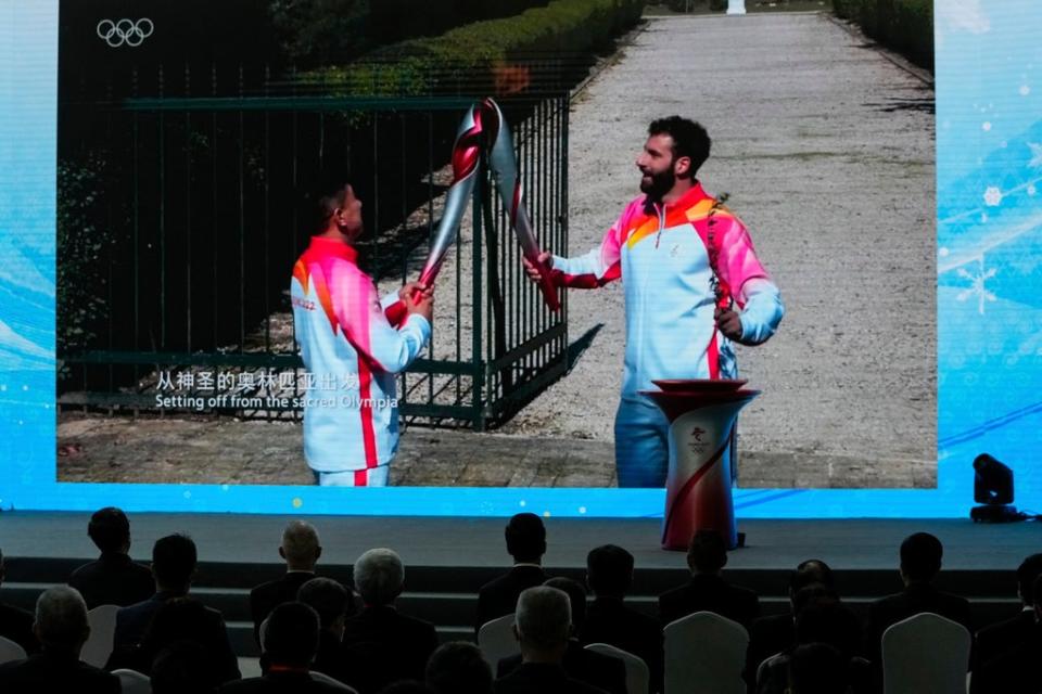 Guests watch video showing first torch bearer, Greek alpine ski racer Ioannis Antoniou, right, pass flame to the second bearer, former Chinese speed skater Li Jiajun (AP)