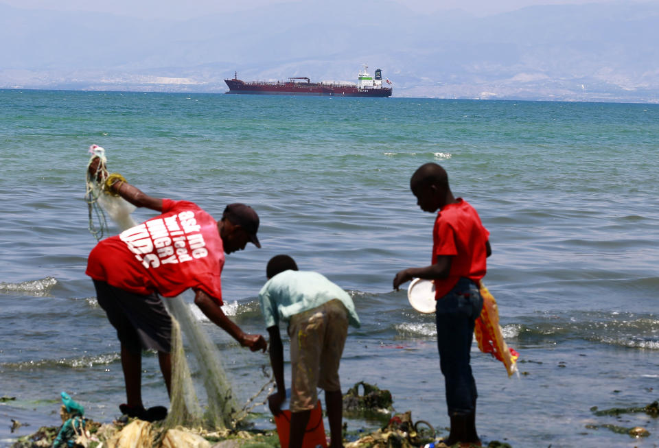 In this April 16, 2019 photo, residents fish while a tanker waits out in the bay to unload its cargo at the Thor terminal in Carrefour, a district of Port-au-Prince, Haiti. The current fuel crisis is helping push Haiti's economy dangerously close to recession. (AP Photo/Dieu Nalio Chery)