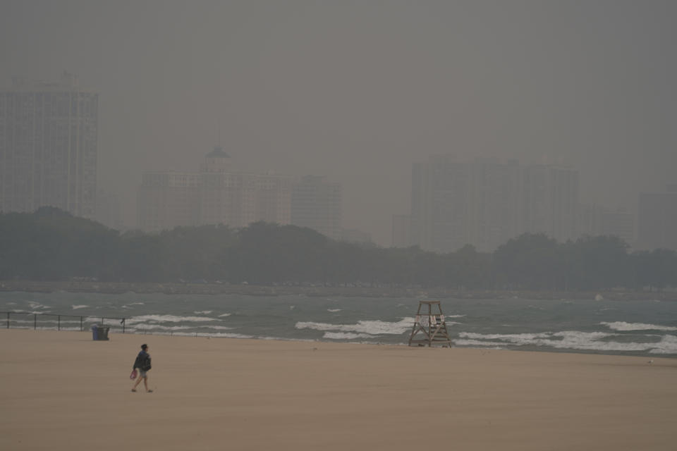 A person walks on Montrose Beach as buildings behind the shore are blanketed in haze from Canadian wildfires Tuesday, June 27, 2023, in Chicago. (AP Photo/Kiichiro Sato)