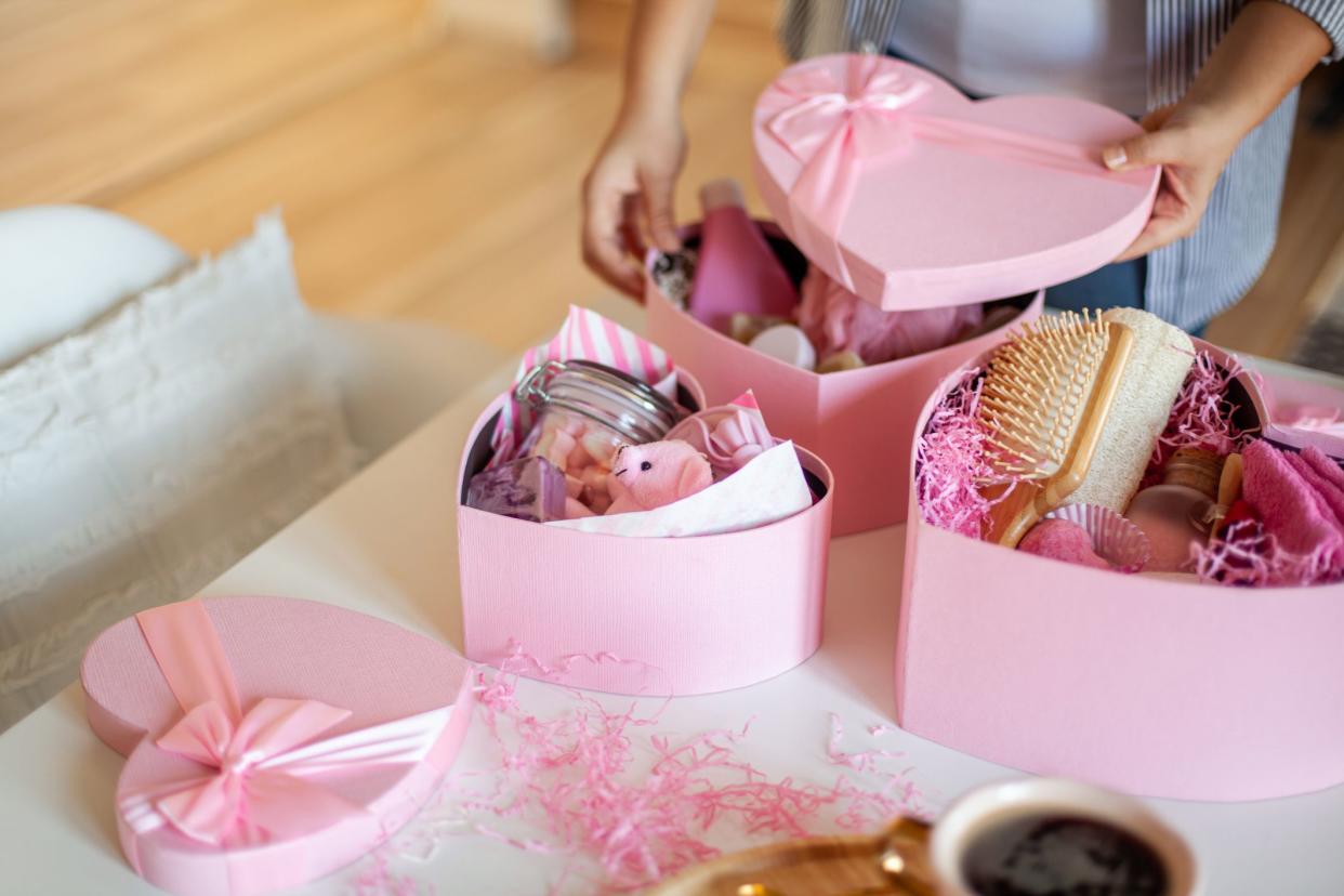 Woman hands holding pink colored heart shaped gift boxes of bath and body products for bridesmaids, bride and as a thoughtful gift for birthdays, anniversary, Valentine's Day, Mother's day, Christmas.