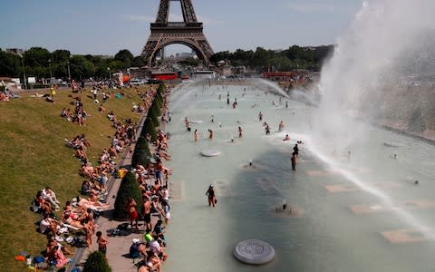 People bathe in the Trocadero Fountain near the Eiffel Tower in Paris during today's heatwave - Credit: AFP