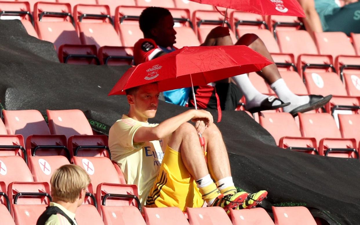 Mesut Ozil shields from the sun under an umbrella in the stands - PA