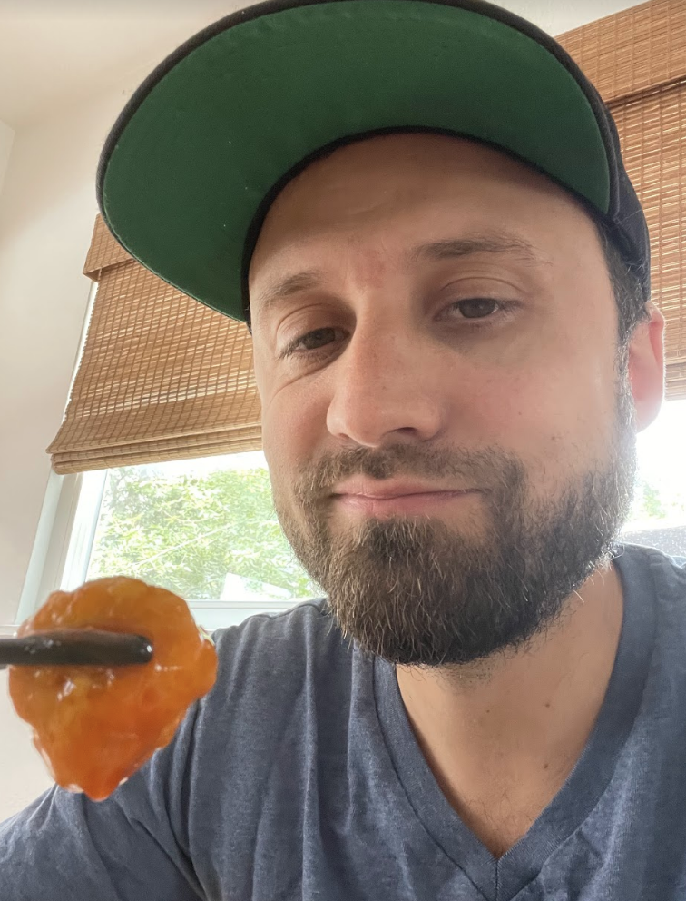 Andy Golder holding a piece of orange chicken with chopsticks.