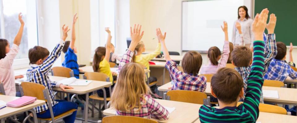 education, elementary school, learning and people concept - group of school kids with teacher sitting in classroom and raising hands