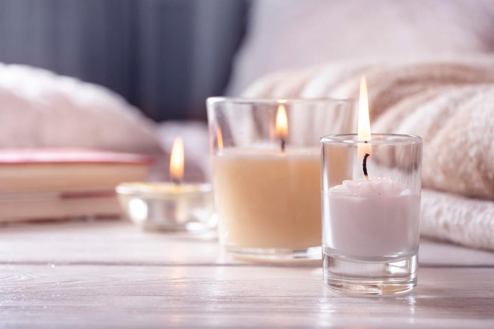 close up on three light colored candles with flames on light wood floor in front of blurry bed and books