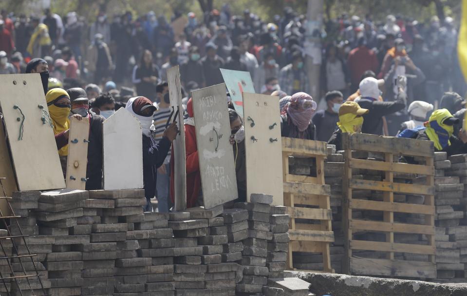 Anti-government demonstrators takes cover behind a barricade during clashes with police in Quito, Ecuador, Saturday, Oct. 12, 2019. Protests, which began when President Lenin Moreno's decision to cut subsidies led to a sharp increase in fuel prices, have persisted for days. (AP Photo/Fernando Vergara)