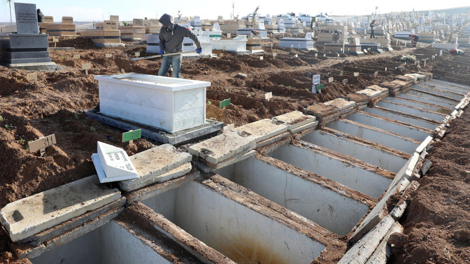 A man backfills a grave in a cemetary alongside more than a dozen other dug gravesites.