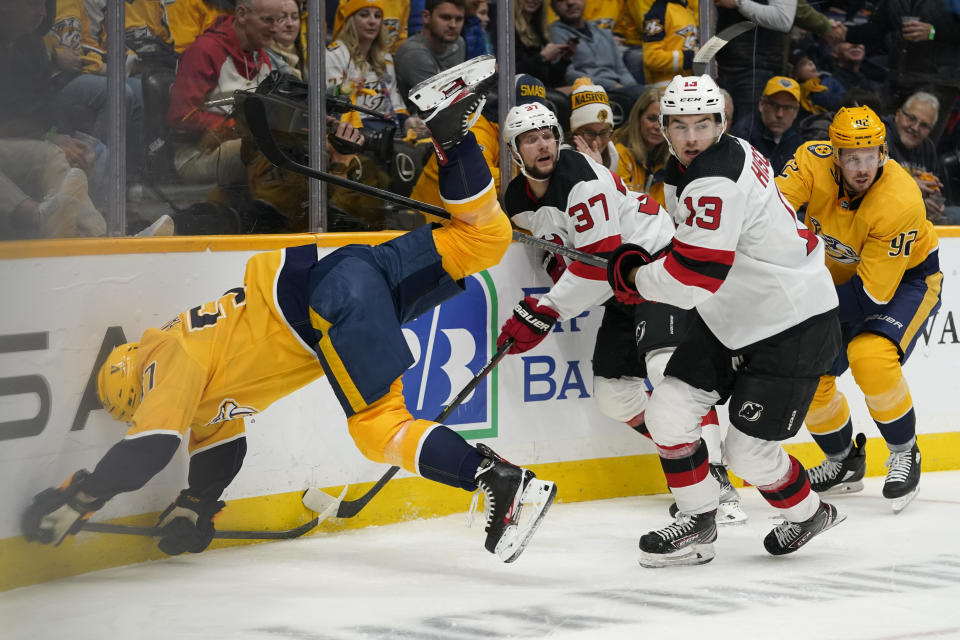 Nashville Predators defenseman Dante Fabbro (57) falls into the boards as New Jersey Devils' Pavel Zacha (37) and Nico Hischier (13) chase the puck in the first period of an NHL hockey game Friday, Nov. 26, 2021, in Nashville, Tenn. (AP Photo/Mark Humphrey)