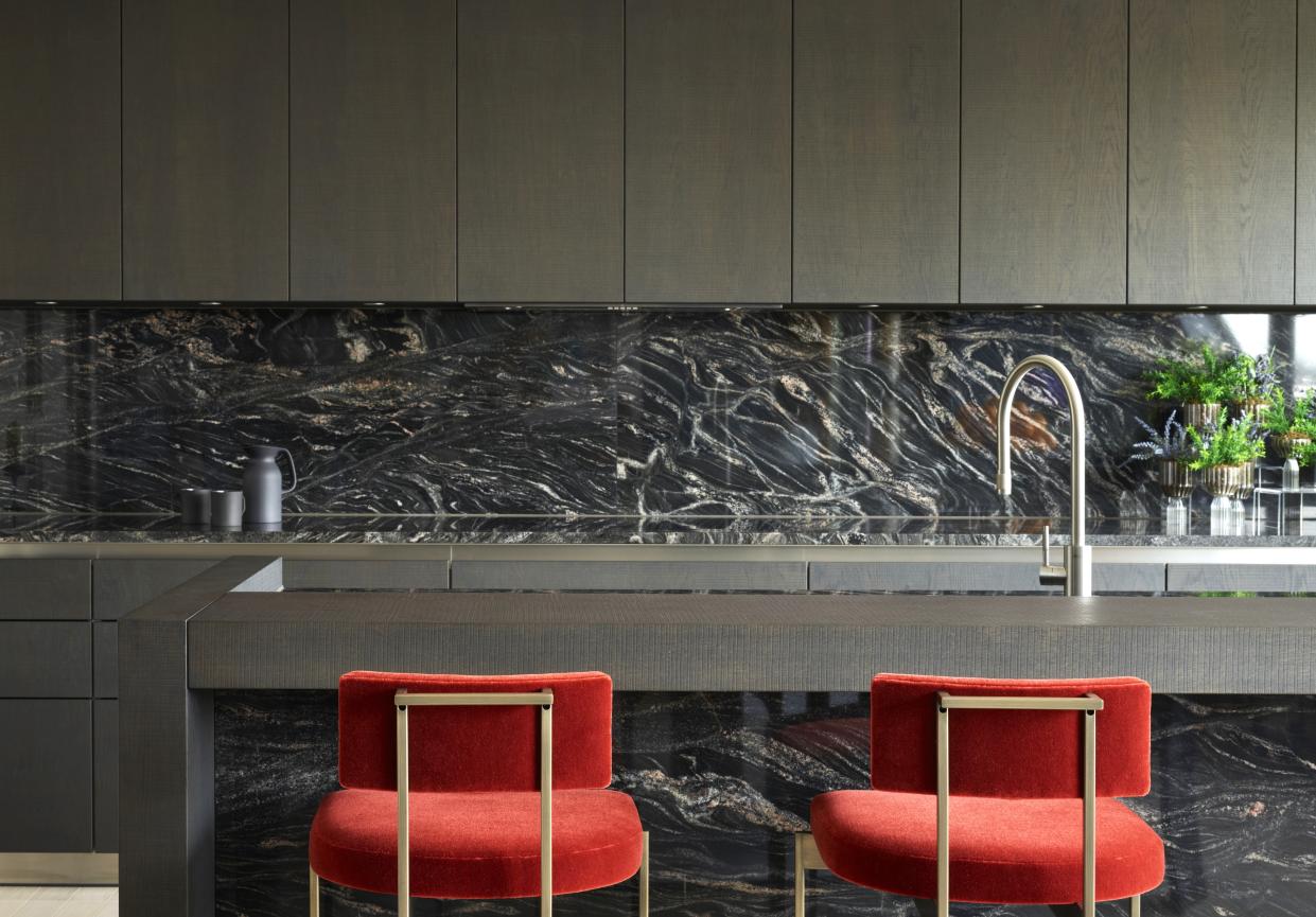  A kitchen with stone backsplash, and red counter stools. 