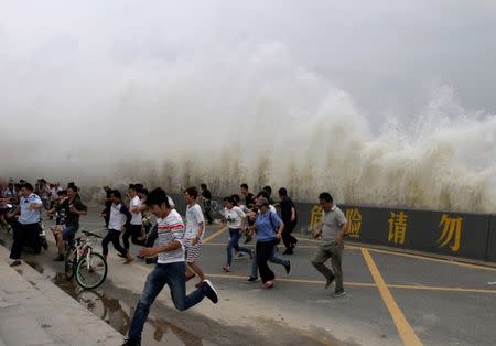 People run way from waves caused by a tidal bore which surged past a barrier on the banks of Qiantang River, in Hangzhou, Zhejiang province, China, October 3, 2016. REUTERS/Stringer