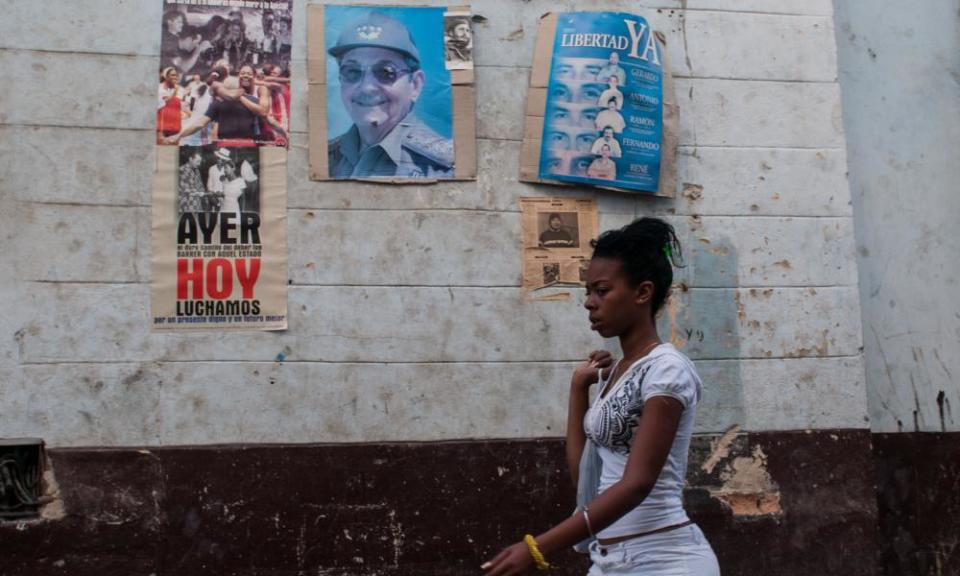 woman walks by Raul Castro posters