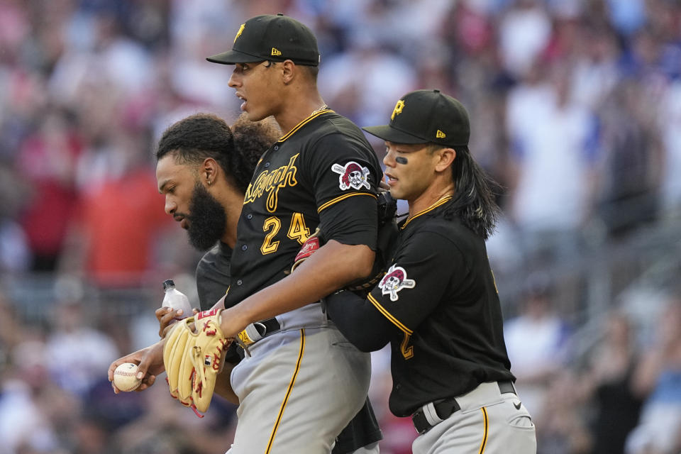 Pittsburgh Pirates starting pitcher Johan Oviedo (24) is held back by teammate, Connor Joe, right, and a grounds crew member in the first inning of a baseball game against the Atlanta Braves, Saturday, Sept. 9, 2023, in Atlanta. (AP Photo/Brynn Anderson)