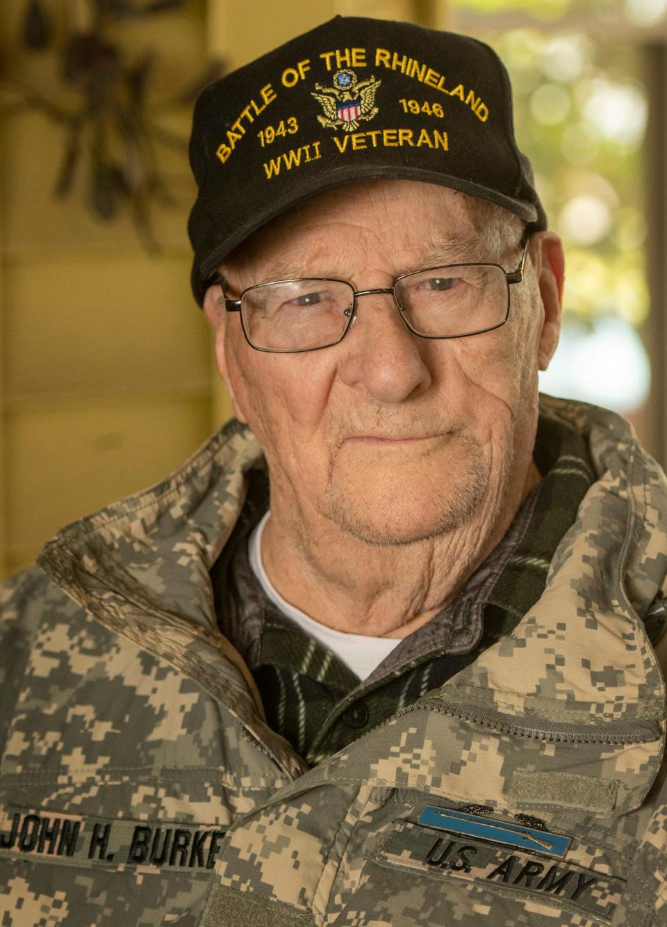 World War II veteran John H. Burke sits on the porch of his Worcester home as workers replace his roof Thursday.