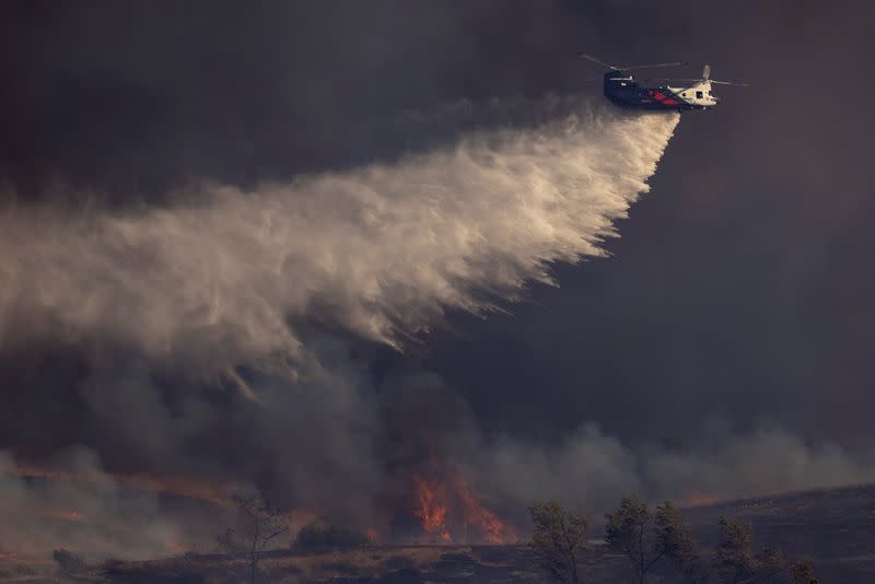 A helicopter makes a water drop on flames as firefighters battle the wind driven Bond Fire wildfire near Lake Irvine in Orange County, California