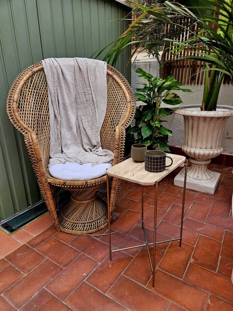 A woven chair sits outside near a coffee table