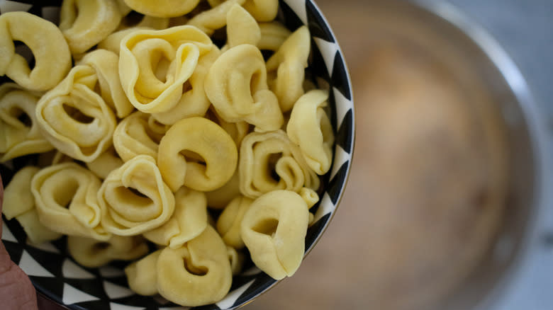 hand holding pasta over soup