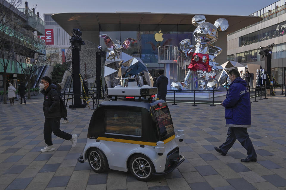 A police robot vehicle patrols past masked visitors at an outdoor shopping center in Beijing, Thursday, Jan. 5, 2023. As COVID-19 rips through China, other countries and the WHO are calling on its government to share more comprehensive data on the outbreak, with some even saying many of the numbers it is reporting are meaningless. (AP Photo/Andy Wong)