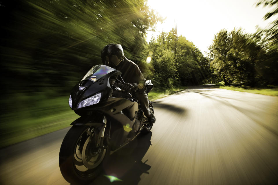 Person riding sport bike in black on private road covered by trees.