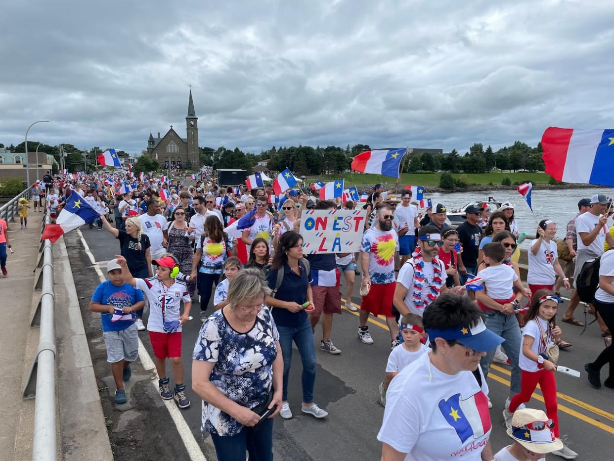 People marched across the bridge on Acadie Street, Route 134, in Bouctouche for a National Acadian Day tintamarre, a traditional Acadian parade where people try to make as much noise as possible. (Alexandre Silberman/CBC - image credit)