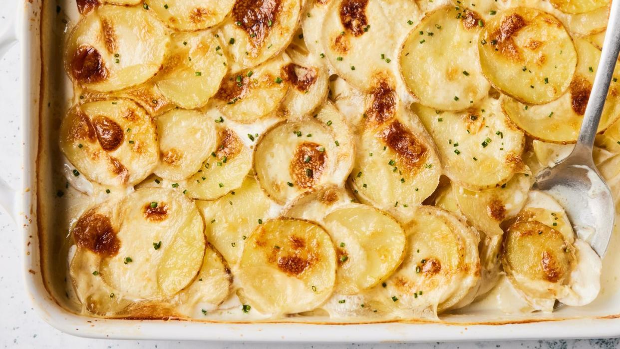 scalloped potatoes in a white baking dish with a silver serving spoon