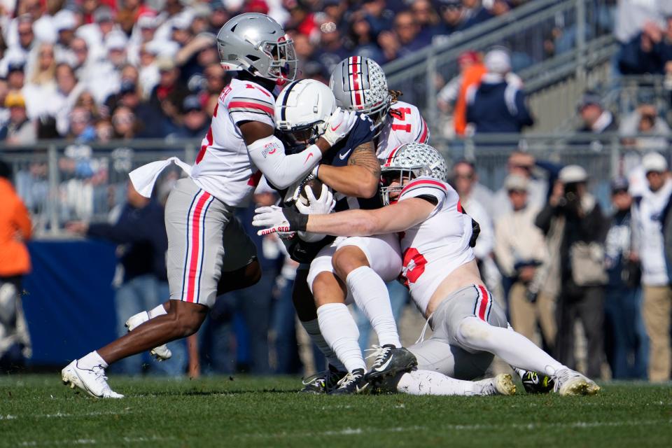 Ohio State safety Tanner McCalister (15), safety Ronnie Hickman (14) and linebacker Tommy Eichenberg (35) tackle Penn State wide receiver Parker Washington (3) during the first half at Beaver Stadium.