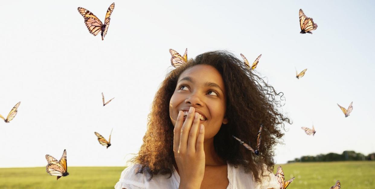 african woman standing among butterflies in meadow