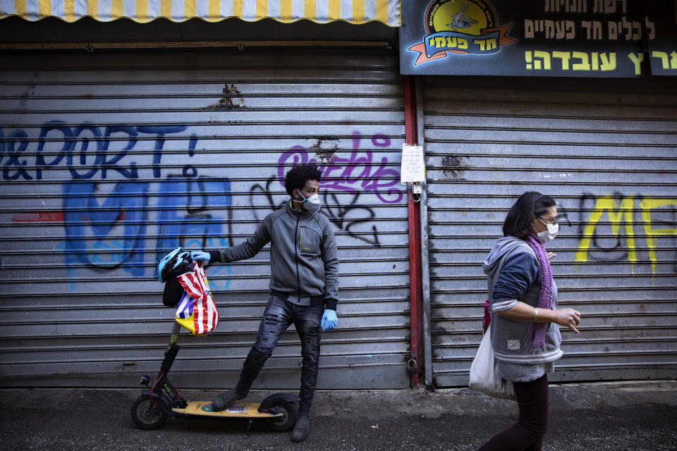 People wear face masks at a closed food market, in Tel Aviv, Israel, Sunday, March 22, 2020. Police officers ordered owners to shut down their shops at the food market in order to reduce the spread of the coronavirus. (AP Photo/Oded Balilty)