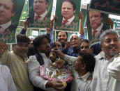 Supporters of Pakistani Prime Minister Nawaz Sharif hold pictures of him and distribute sweets to celebrate the suspension of prison sentences of Sharif, his daughter and son-in-law, in Lahore, Pakistan, Wednesday, Sept. 19, 2018. The Islamabad High Court set them free on bail pending their appeal hearings. The court made the decision on the corruption case handed down to the Sharifs by an anti-graft tribunal earlier this year. (AP Photo/K.M. Chaudary)