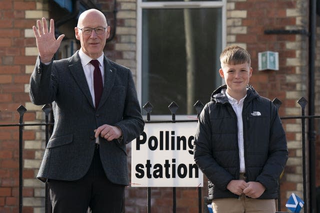 John Swinney waving while standing alongside his son Matthew outside a polling station