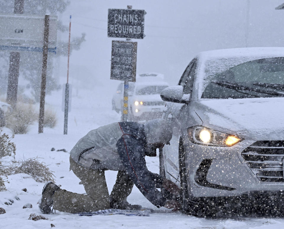 Evan Freedman, from Los Angeles, puts snow chains on his vehicle as heavy snow falls on Highway 2 near Wrightwood, Calif., on Monday, Dec. 12, 2022. (Will Lester/The Orange County Register via AP)