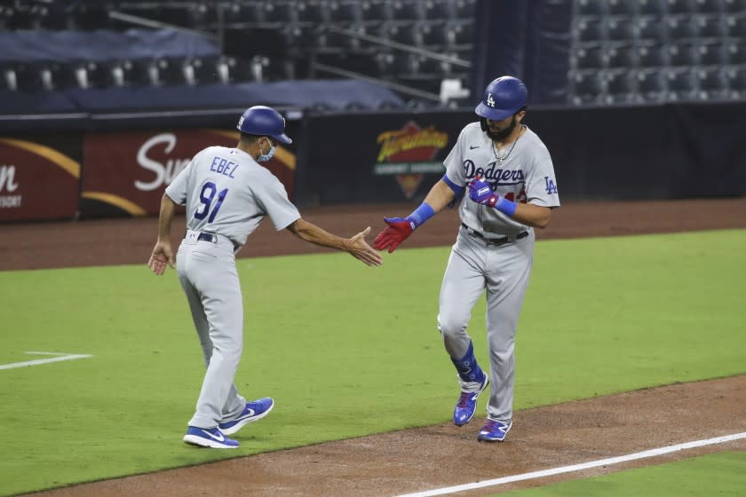 Los Angeles Dodgers third base coach Dino Ebel high fives Edwin Rios as rounds third after hitting a solo home run off San Diego Padres starting pitcher Zach Davies in the fifth inning of a baseball game Tuesday, Sept. 15, 2020, in San Diego. (AP Photo/Derrick Tuskan)