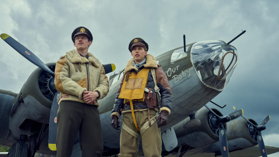 Two pilots stand in front of a World War 2 era plane