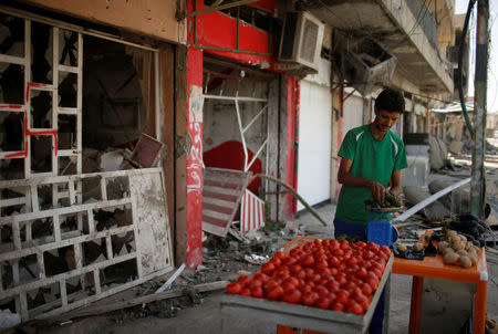 An Iraqi vendor sells vegetables outside a destroyed shop, in western Mosul, Iraq July 31, 2017. REUTERS/Suhaib Salem