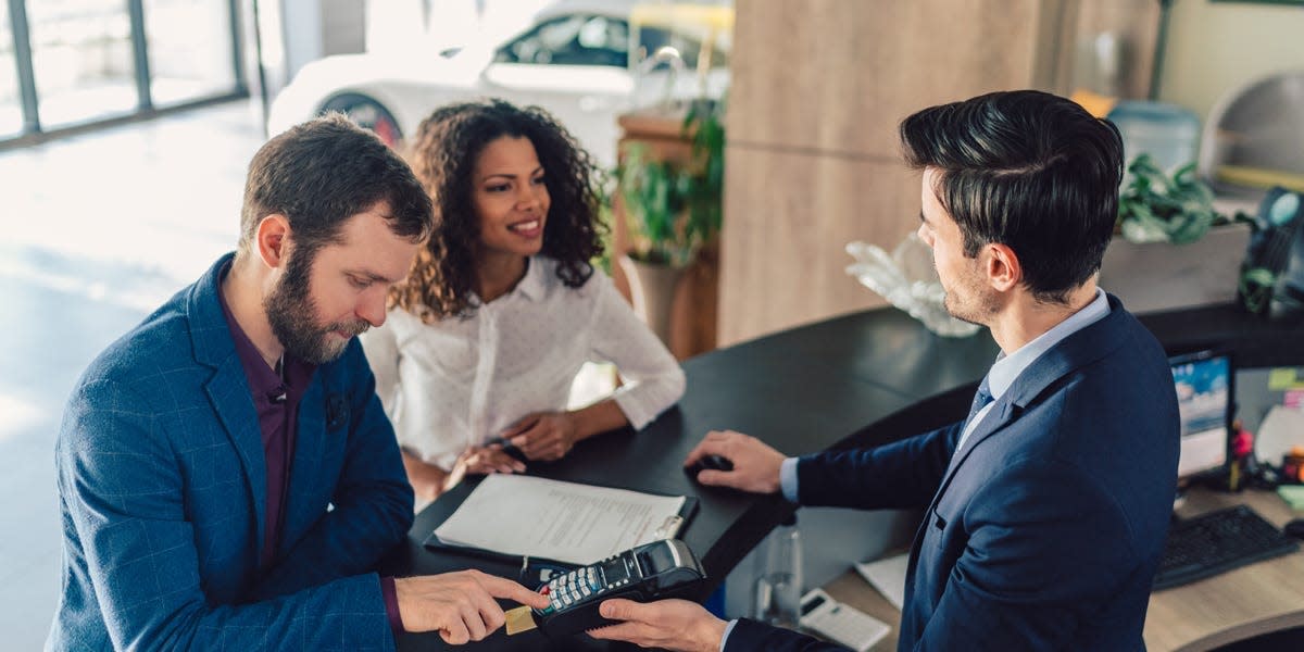 A photo of a young couple paying for a new car at a dealership.