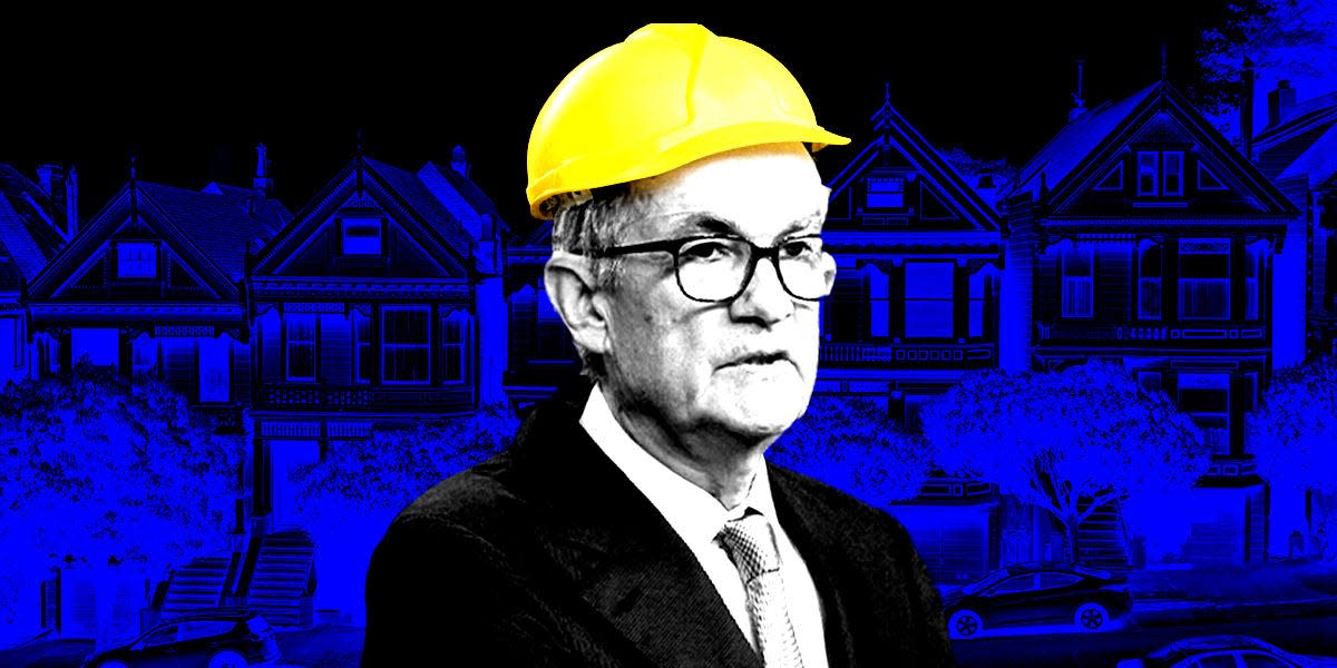 Jerome Powell in a hard hat in front of. houses.