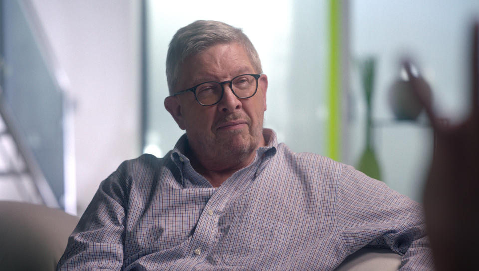 Former Brawn GP co-founder Ross Brawn sits on a sofa. He's wearing black glasses and a grey shirt.