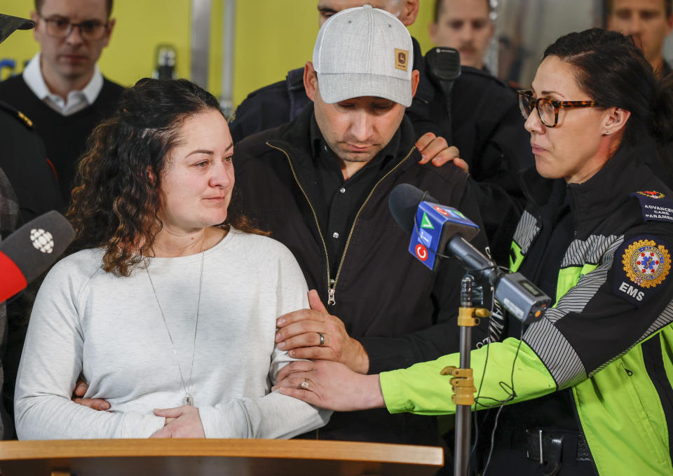Paramedic Jayme Erickson, left, who was called to a crash last week and didn't know she was trying to save her own daughter because the injuries were too severe, is comforted by her husband Sean Erickson, center, and friends as she speaks to the media in Airdrie, Alberta, Tuesday, Nov. 22, 2022. (Jeff McIntosh/The Canadian Press via AP)