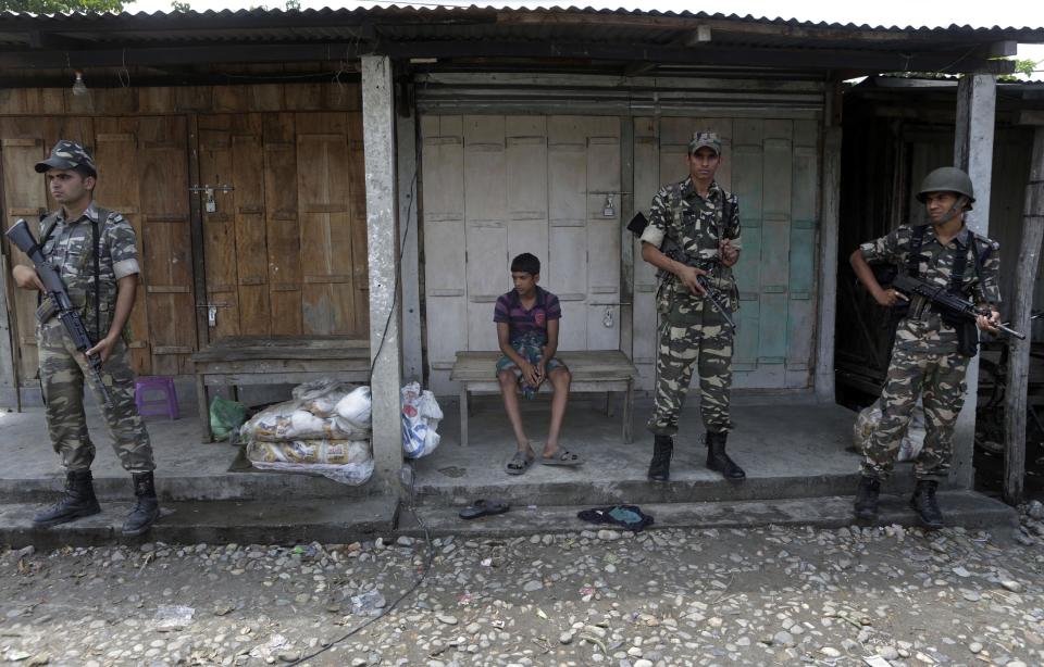A villager sits on a bench as Indian security officers stand guard at violence-affected Narayanguri village, in the northeastern Indian state of Assam, Saturday, May 3 2014. Police in India arrested 22 people after separatist rebels went on a rampage, burning homes and killing dozens of Muslims in the worst outbreak of ethnic violence in the remote northeastern region in two years, officials said Saturday. (AP Photo/Anupam Nath)
