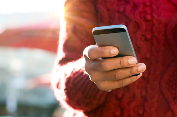 A hand holding and typing on a smartphone.