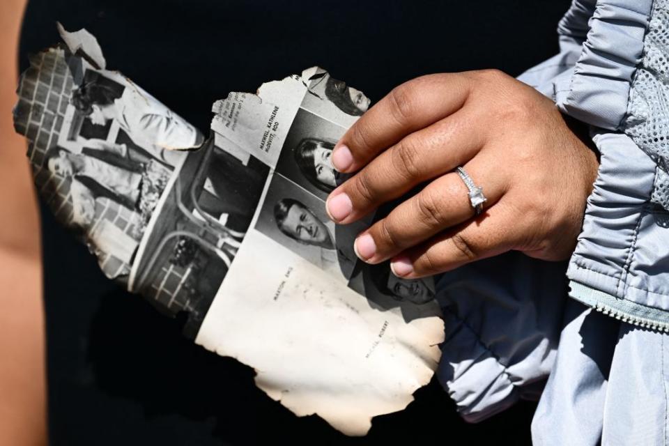 Davilynn Severson holds a page of a yearbook as she looks for belongings through the ashes of their family's home in the aftermath of a wildfire in Lahaina.