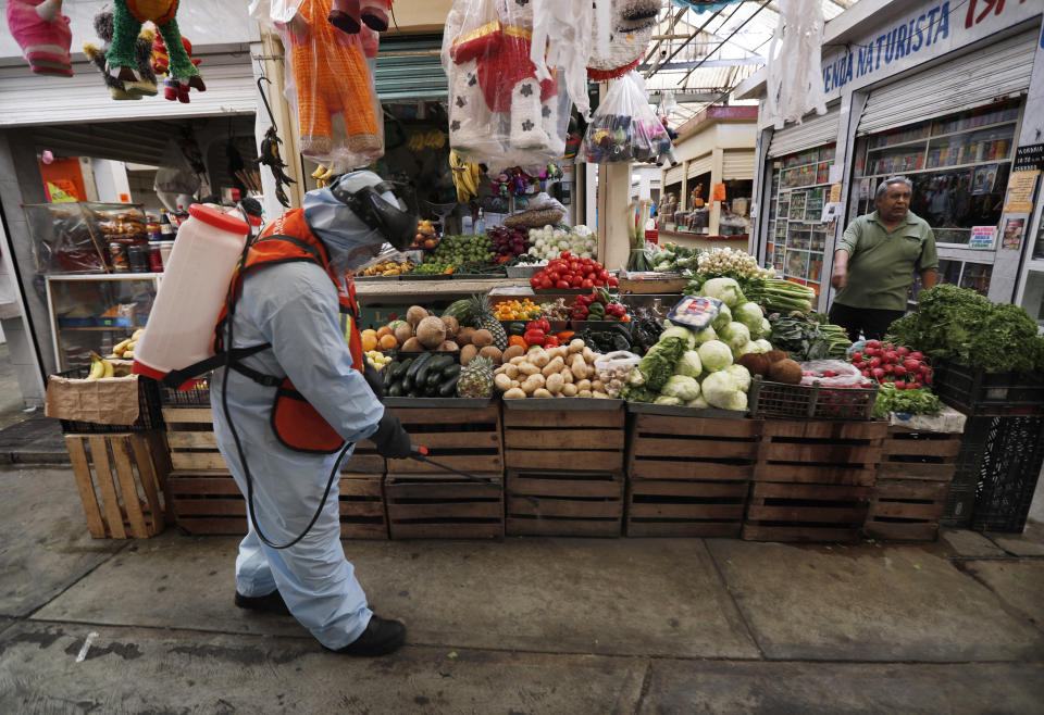 A member of a cleaning team wearing a protective mask and suit disinfects a showcase where fruit is sold, as a preventive measure against the spread of the new coronavirus, at the Iztapalapa market, in Mexico City, Thursday, April 2, 2020. Mexico has started taking tougher measures against the new coronavirus, but some experts warn the country is acting too late and testing too little to prevent the type of crisis unfolding across the border in the United States. (AP Photo/Marco Ugarte)