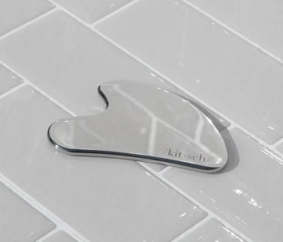 A Kitsch brand stainless steel facial massage tool on tiled surface
