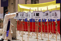 A Catholic priest sprinkles holy water on signs showing the photos and names of health workers who have died of COVID-19 during a ceremony in their honor in Caracas, Venezuela, Thursday, Sept. 10, 2020. (AP Photo/Ariana Cubillos)