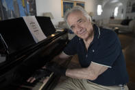 Brazilian pianist Joao Carlos Martins poses for pictures wearing bionic gloves, at his home in Sao Paulo, Brazil, Wednesday, Jan. 22, 2020. Martins, 79, was for decades Brazil's most acclaimed pianist, but an accident an a degenerative disease forced him to stop playing with both hands since 1998. That changed a few months ago when a new friend came to him with a pair bionic gloves that suit him perfectly. He can now play again with nine out of ten fingers. (AP Photo/Andre Penner)