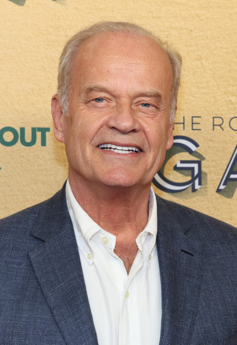 A man smiling in a blazer and open-collar shirt at an event