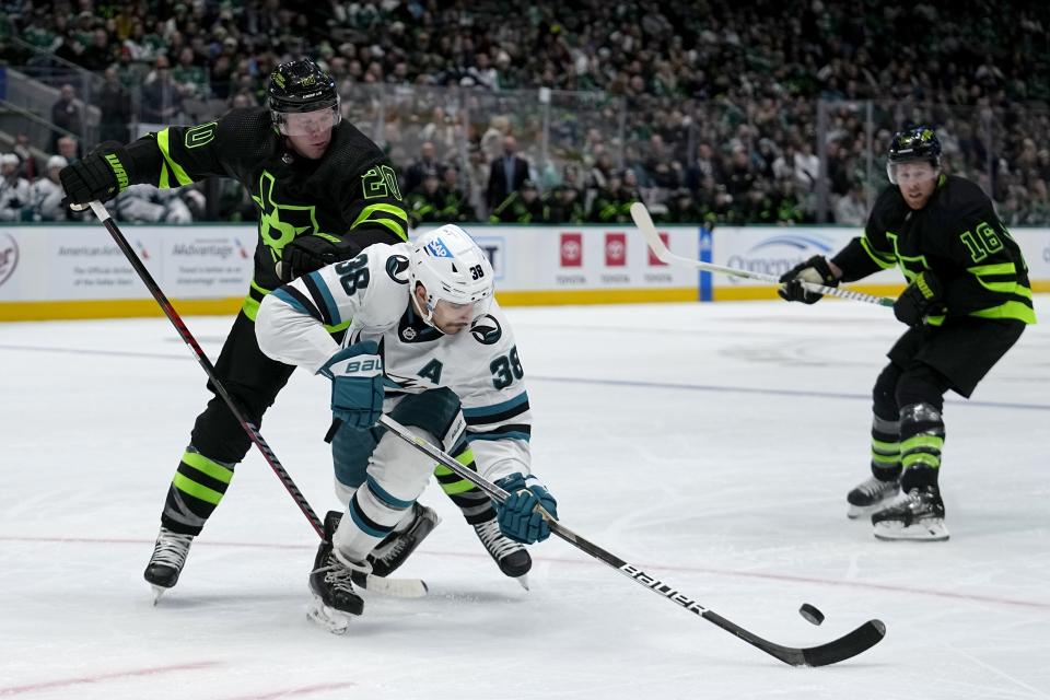 San Jose Sharks defenseman Mario Ferraro (38) attempts to gain control of the puck under pressure from Dallas Stars defenseman Ryan Suter (20) and Joe Pavelski (16) in the first period of an NHL hockey game in Dallas, Friday, Nov. 11, 2022. (AP Photo/Tony Gutierrez)