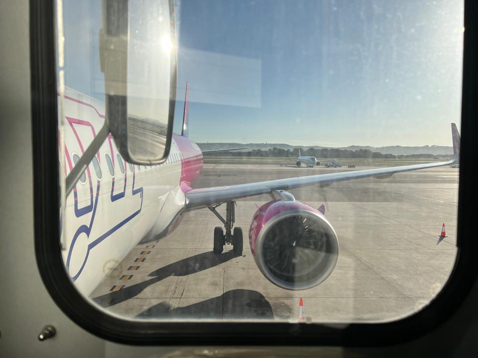 The side of a Wizz Air Airbus A321neo viewed from a jet bridge with a wing mirror in the foreground.