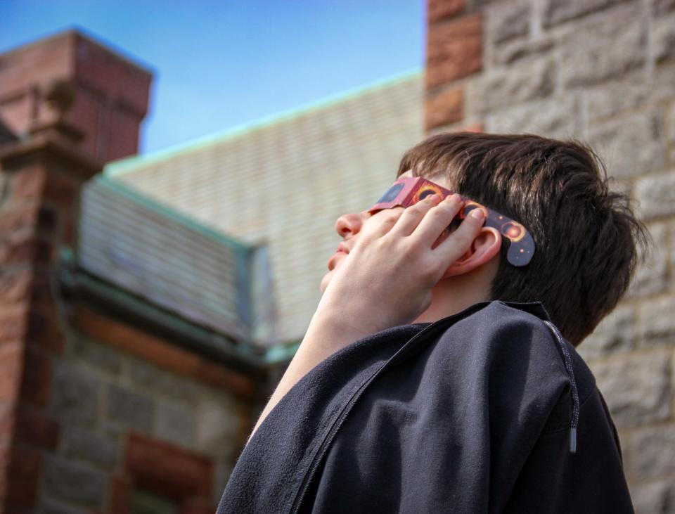 Matthew Crawford wears a pair of special glasses to view the solar eclipse outside Swansea Free Public Library on April 8, 2024.