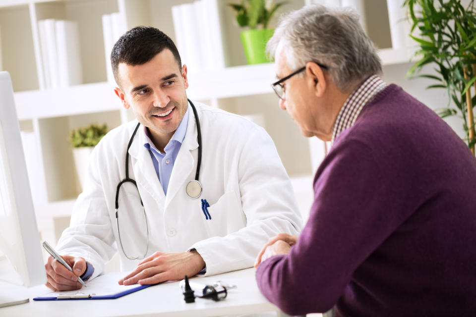 A male doctor talking to a male patient while writing on a clipboard..