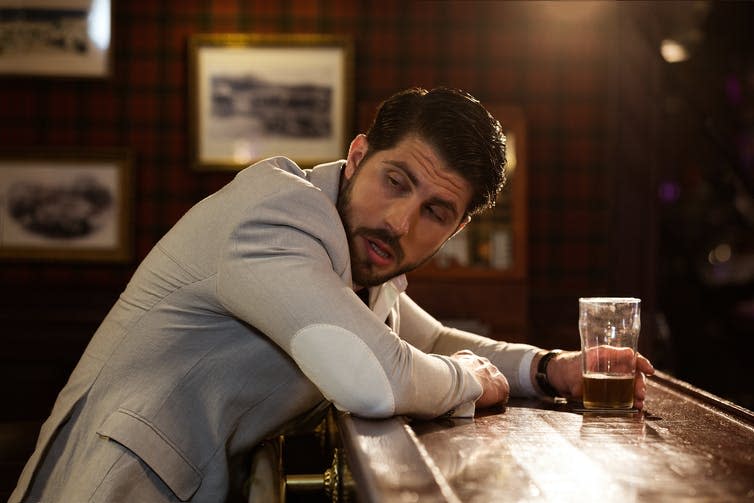 Young drunk man sitting at the counter in a pub or a bar and drinking beer